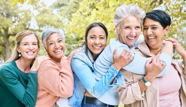 50 AÑOSY MAS Friends, park and group of women hug enjoying bonding, quality time and relax in nature together. Diversity, friendship and portrait of happy senior females with smile, embrace and peace outdoors