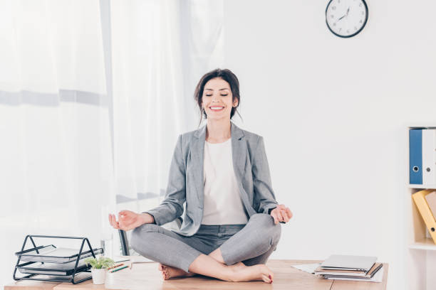 ejecutiva haciendo yoga beautiful smiling businesswoman in suit sitting on desk and meditating in Lotus Pose in office