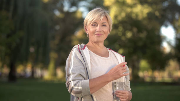 Pretty middle aged woman drinking water in park, keeping water balance, health Pretty middle aged woman drinking water in park, keeping water balance, health